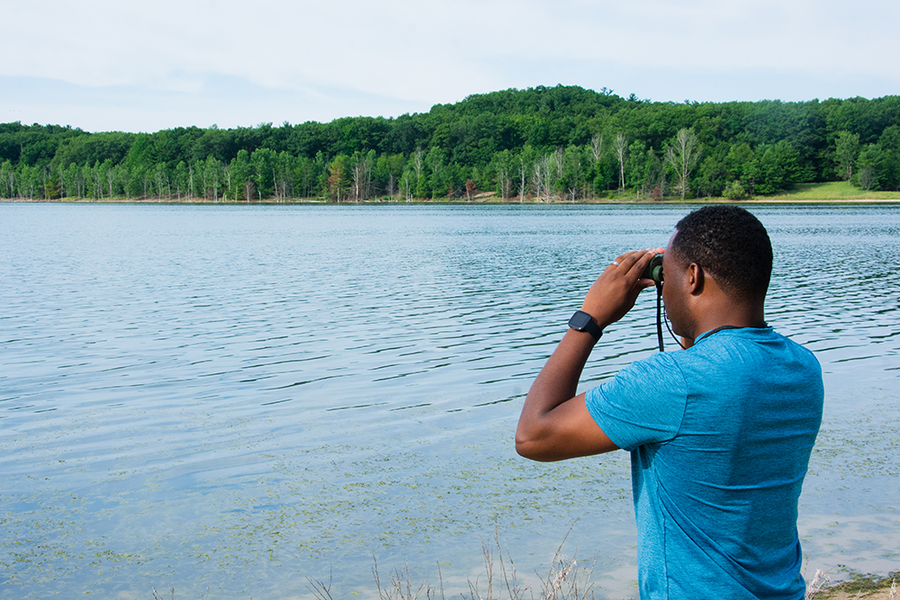 Man looks at south lake at Dune Harbor Park through binoculars