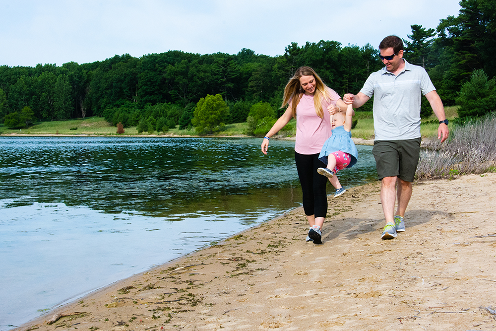 Woman and man lift their young child between them as they walk along the shore of the south lake at Dune Harbor County Park.