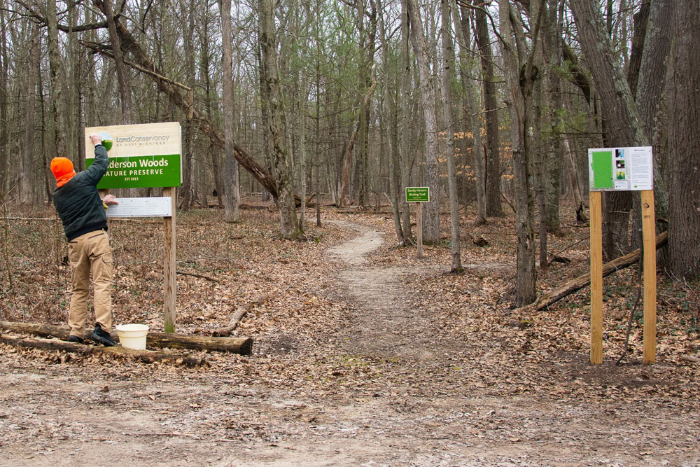 Volunteer cleans preserve sign at Anderson Woods Nature Preserve.
