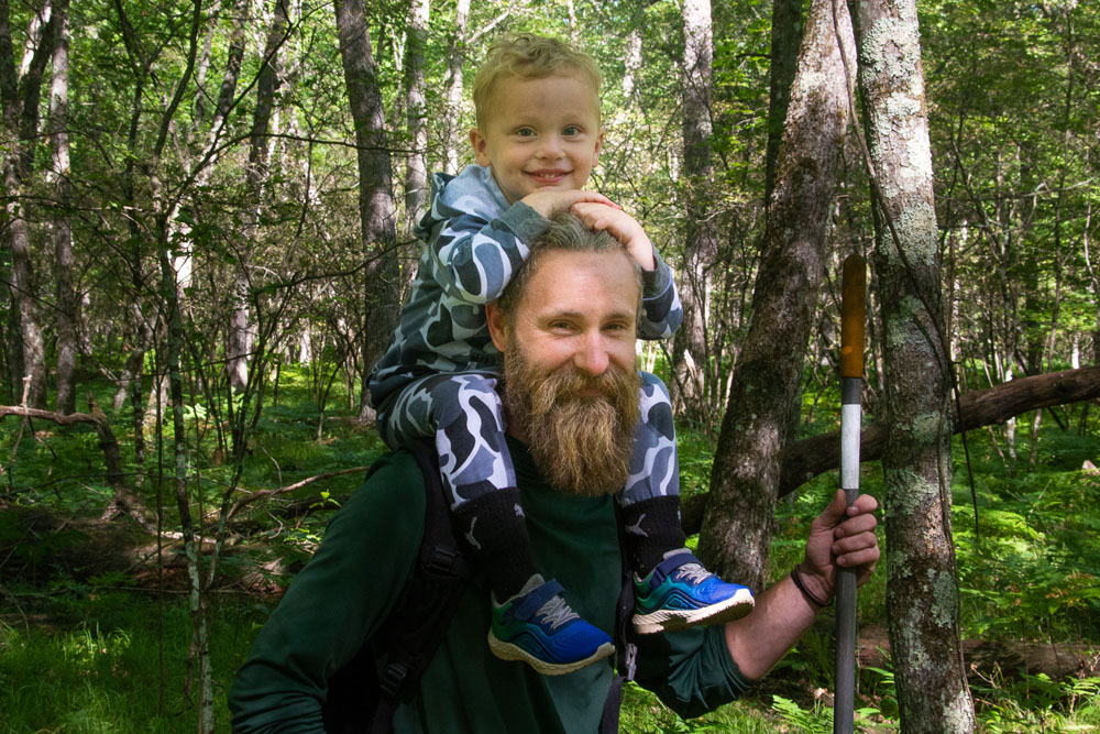 Small child sits on his father's shoulders at Upriver Nature Preserve trail building workday